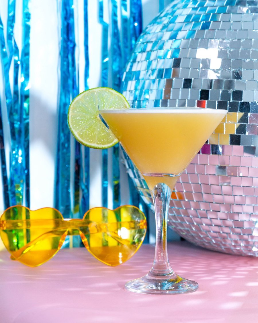 Yellow disco cocktail with lime garnish in front of a mirror ball
