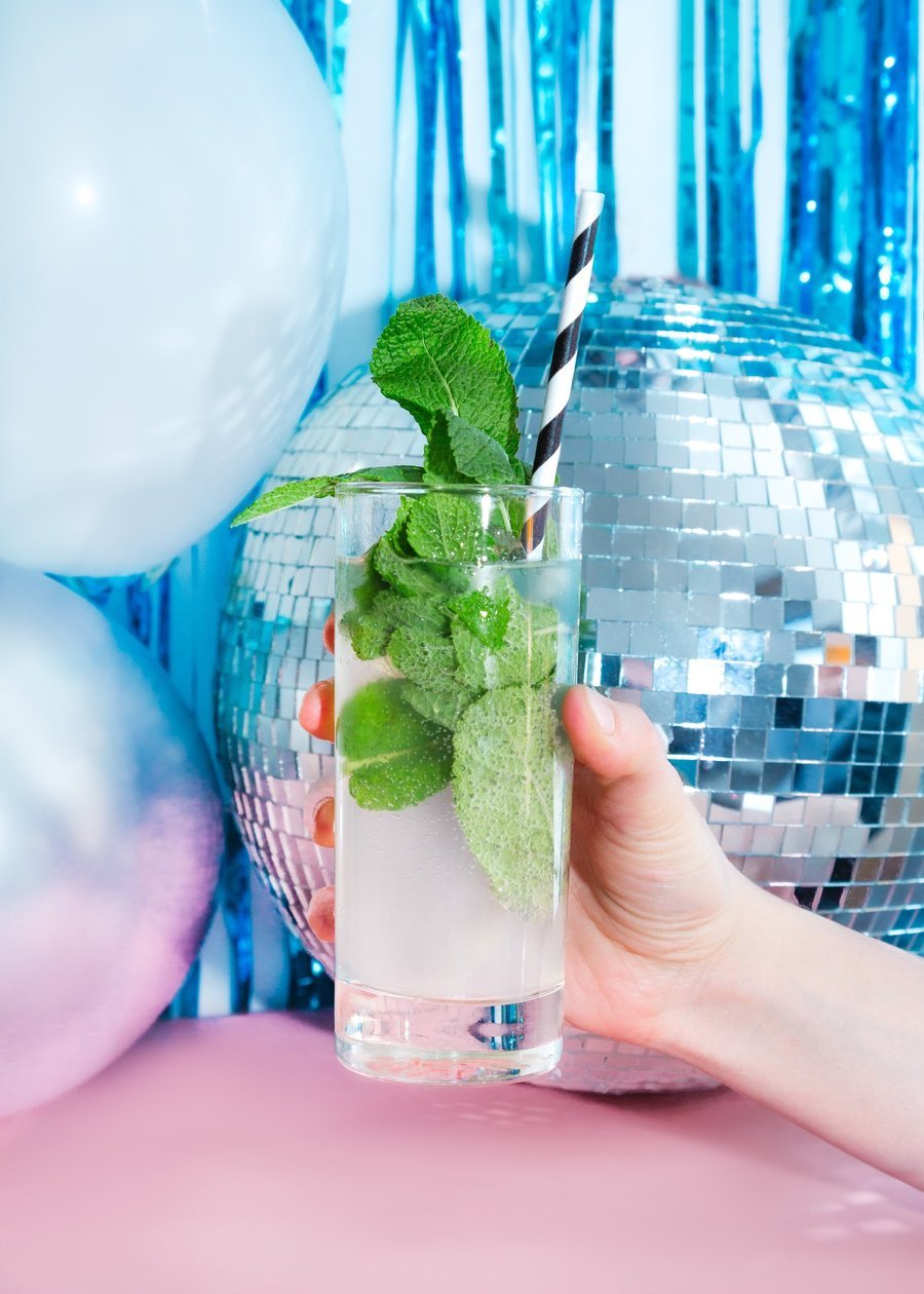 Guest holding a mint disco cocktail beside a mirror ball